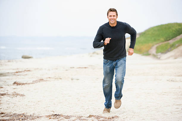 mann läuft am strand lächelnd - approaching stock-fotos und bilder