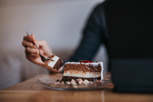 Close up shot of an unrecognizable woman sitting at the table and eating a piece of cake.
