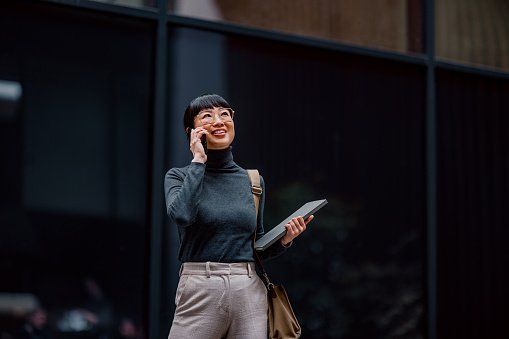 Modern Smiling Japanese Businesswoman Having a Phone Call While Walking in the City