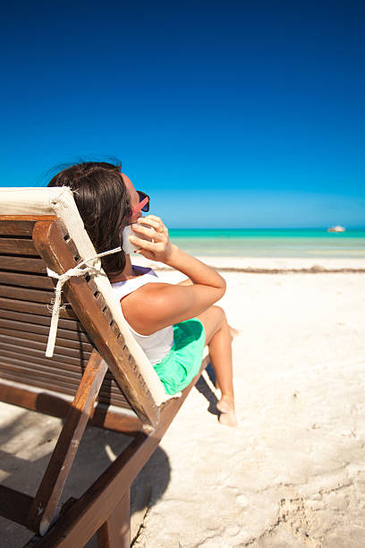 istock Young woman talking on phone while sitting at beach lounger 179012705