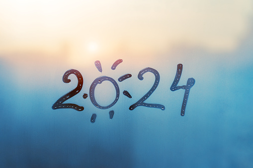 numbers 2024 of new year with shape of sun paint with finger on splashed by rain foggy glass on blue sunset window