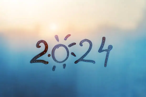 Photo of numbers 2024 of new year with shape of sun paint with finger on splashed by rain foggy glass on blue sunset window