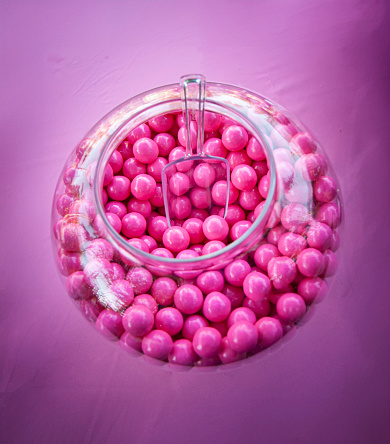 Close up of pink gumballs in a glass bowl with a plastic scoop