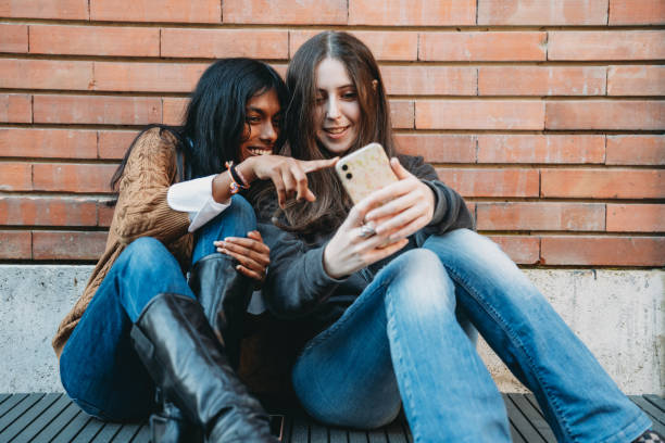 istock Two friends are sitting against a brick wall using a mobile phone together 1790142855