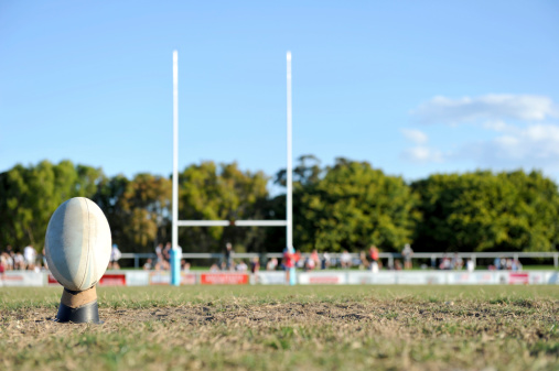 Rugby ball placed on a kicking tee with goal posts in the background
