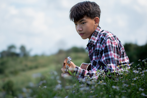 Asian boy plays ukulele in the backyard, hobby and relaxing of child concept.