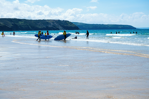 Perranporth, United Kingdom - June 1 2022: People swimming or paddle boarding on sandy beach in Cornwall, South West, United Kingdom. View of the beach, blue sea and cliffs. Selective focus