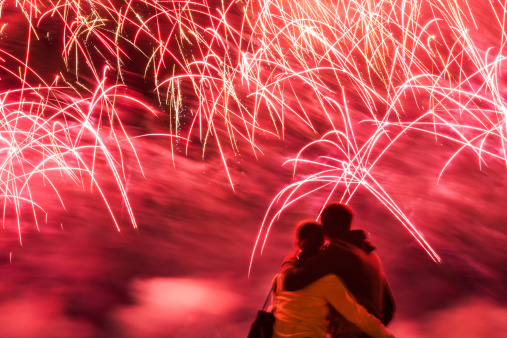 Big fireworks with young romantic couple in love in front, holding each other and watching the show