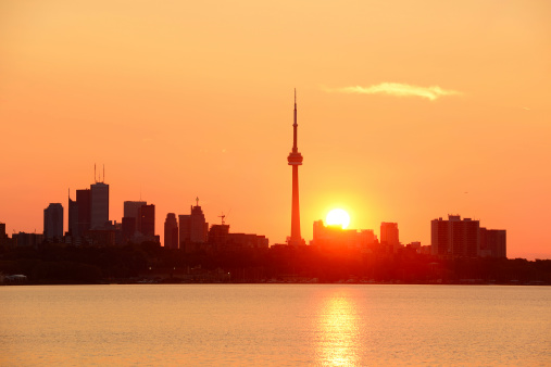 Toronto sunrise silhouette over lake with red tone.