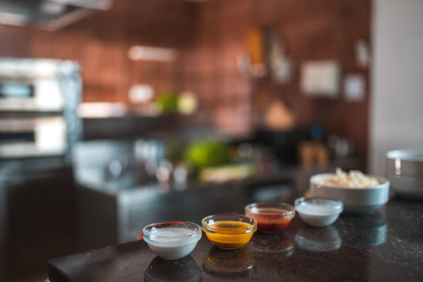 Close up shot of a variety of sauces and seasonings can be seen on the counter. Small containers are in focus while the kitchen is in the background.