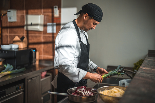 Side shot of a Japanese male chef preparing fresh ingredients. He is washing and cleaning red cabbage and leek.