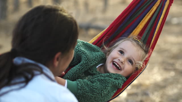 Mom and daughter enjoy autumn nature in hammock swing.