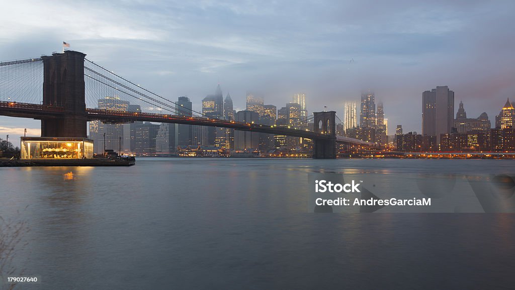 Brooklyn Bridge and Lower Manhattan at dusk, New York Brooklyn Bridge and New York skyline across the East River at twilight on a foggy day. Architecture Stock Photo