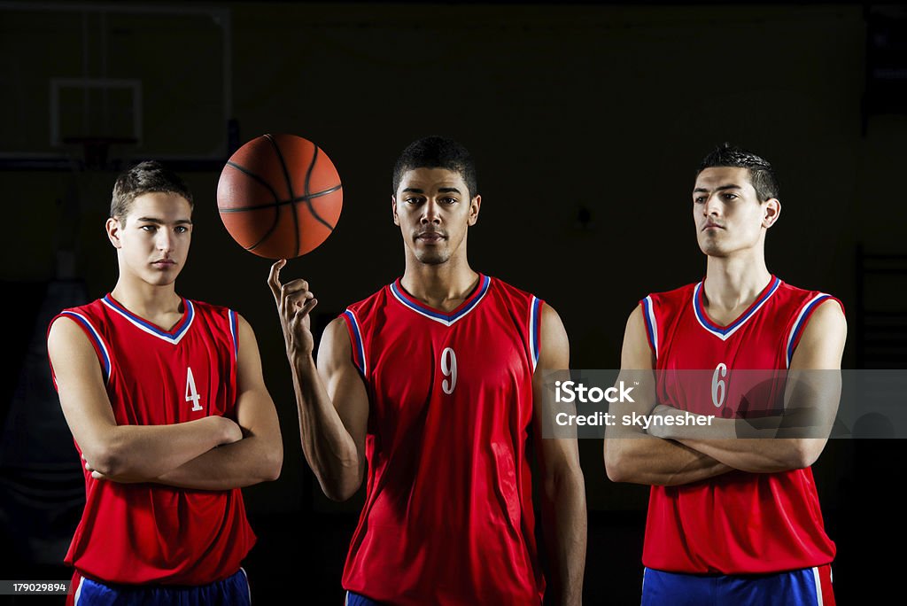 Basketball players. Three basketball players. One of them is looking at the camera while holding a ball.    Basketball Team Stock Photo