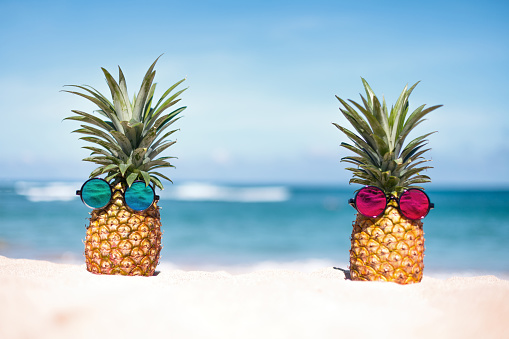 Two pineapples with trendy sunglasses on the beach