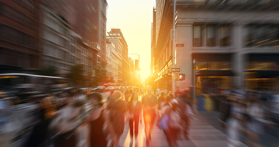 Crowds of people walking across the busy intersection at 23rd Street and 5th Avenue in New York City with the light of sunset background and motion blur effect