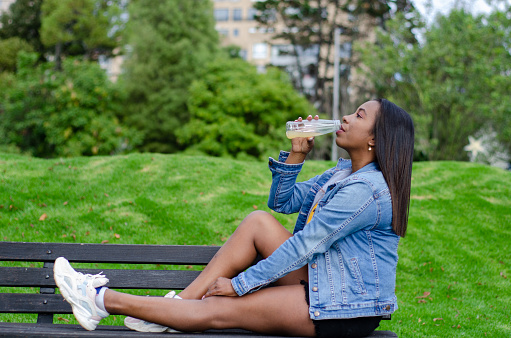 portrait of black woman sitting and drinking from a bottle in public park