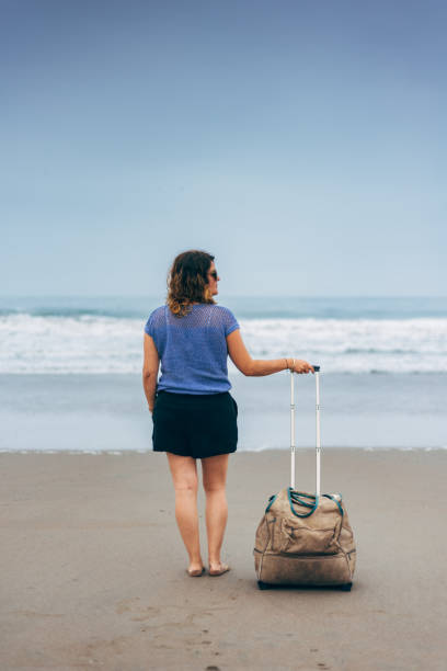 istock vertical image of a Woman on the beach with suitcase. Copy space 1790398763