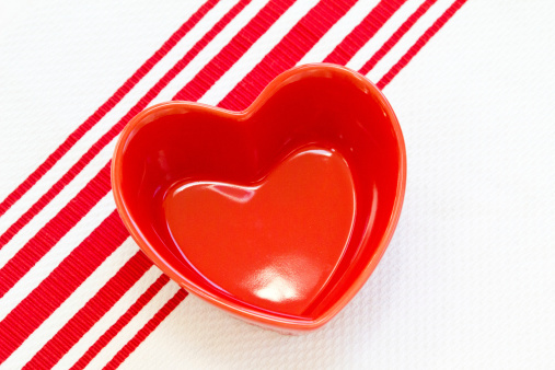 An empty red heart dish on a red striped tea towel