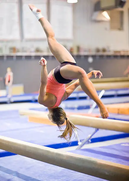 Female gymnast performing a flip on a balance beam. She is catpured in mid-air. High shutter and shallow DOF needed to freeze the action. Image made possible only with modern, top of the line DSLR.