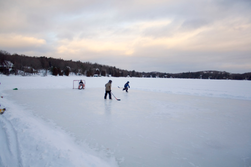 Kids play ice hockey on a frozen lake in a rustic Canadian scene