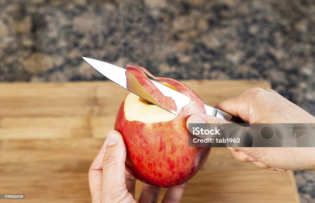 Fresh Apple being peeled with paring Knife Horizontal photo of female hands peeling skin off of apple using a paring knife with bamboo cutting board and stone counter top in background Kitchen Knife Stock Photo