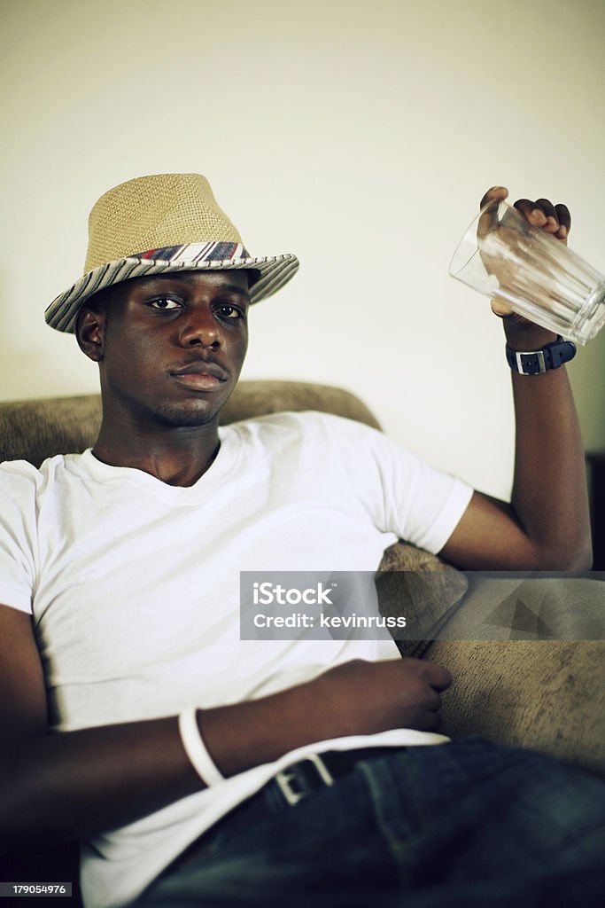 Giovane uomo in un cappello bere sul divano - Foto stock royalty-free di Abbigliamento casual