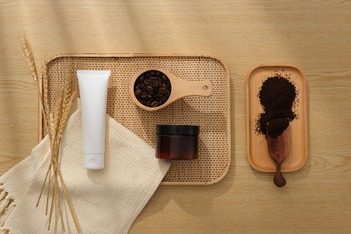 Minimalist creative background for cosmetics or products presentation with coffee ingredient. Plastic tube and amber jar displayed on tray with beans and powder of coffee on wooden background