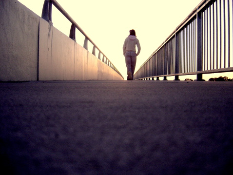 A lonely girl walking along bridge.