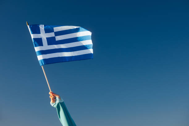 istock Hand Waiving a Greek Flag on a Blue Sky 1790575500