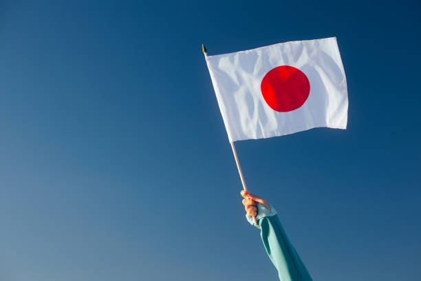 istock Hand Waiving a Japanese Flag on a Blue Sky 1790576006