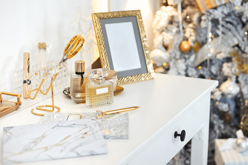 Close-up fashionable and beautiful women's dressing table with white and gold color accessories on the background of a Christmas tree.