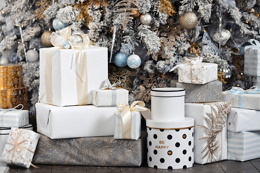 A lot of xmas presents. Close-up christmas morning with many gift boxes under a luxury rich decorated xmas tree in white, silver gold colors. Winter holiday mood.