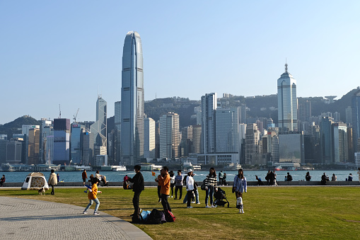 People relaxing on a meadow at West Kowloon cultural district park, facing Hong Kong island skyline.