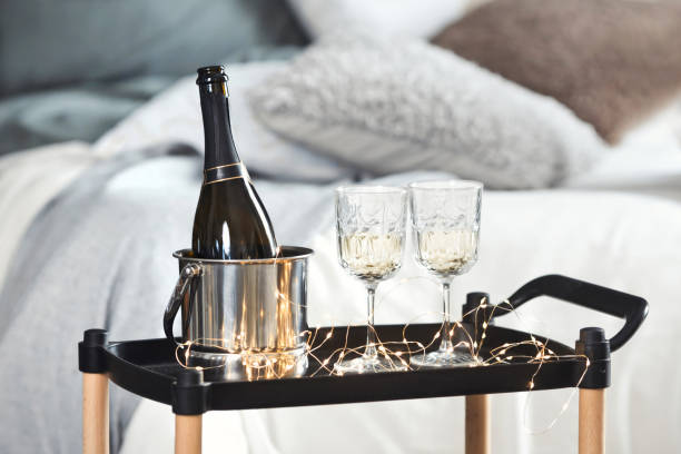 botella de champán en primer plano en un cubo y dos copas de vino de cristal en una bandeja con el telón de fondo de una cama acogedora y cómoda con almohadas. cita romántica para dos. feliz día de san valentín - suite de hotel fotografías e imágenes de stock