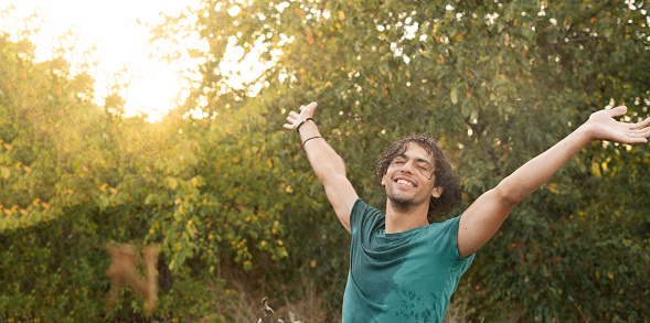 Happy young Arab man enjoying freedom under raindrops enjoying the coolness of summer at sunset. Copy space. Banner
