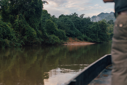 Unrecognizable man standing out of frame on a canoe floating down a jungle river in Kanchanaburi province of Thailand.