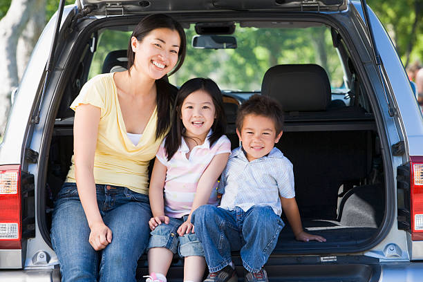 Woman with two children sitting in back of van smiling Woman with two children sitting in back of van smiling. Mother and children looking directly at the camera. family-van-driving stock pictures, royalty-free photos & images
