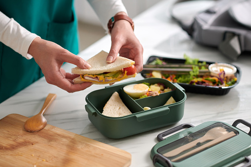 Nurse packing lunch for work, putting sandwich, salad and cut fruits in plastic container