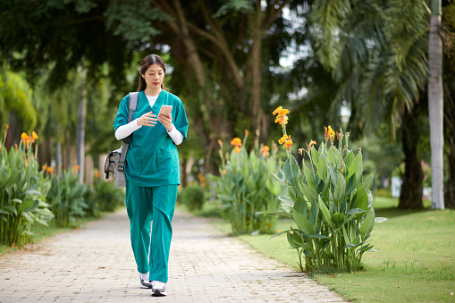 Medical nurse checking notifications on smartphone when walking to workplace