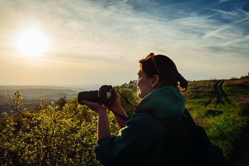 Adult woman hiker with camera taking pictures of beautiful nature. Professional female photographer working outdoors.