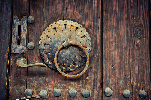Elements of a vintage wooden door. Old wood, rusty forged iron handle, iron nails, rivets. Vintage background with copy space.