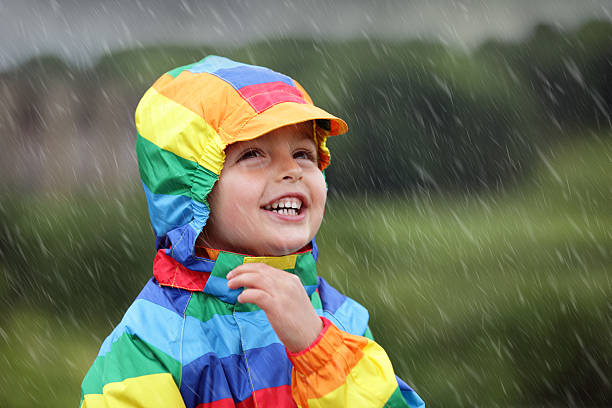 A young boy outside in the rain Little boy enjoying the rain dressed in a rainbow colored raincoat only boys stock pictures, royalty-free photos & images