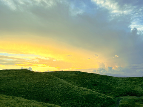 the nature mountain ridge landscape yellow sunrise or sunset view is a green grass meadow and highland hill mountain with white cloud cloudy cloudscape on a blue beautiful bright sunlight sky background