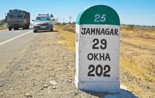 Horizontal color landscape of the 29 kilometers to Jamnagar direction milestone of the Gujarat state highway in India. Stationary vehicle and truck whizzing past under clear blue sky upto the horizon line