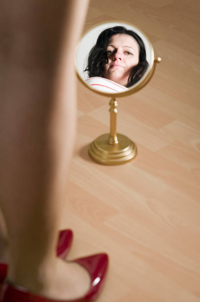 red pomps and mirror artistic portrait of a black-haired woman of middle age: fore feet and lower leg with red high hills on laminate flooring and preceding mirror with mirror image of the head beines stock pictures, royalty-free photos & images