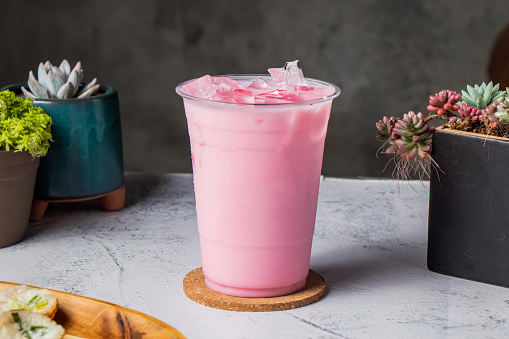 iced strawberry milkshake or rose milk served in disposable glass with ice cube isolated on wooden board side view of taiwanese ice drink