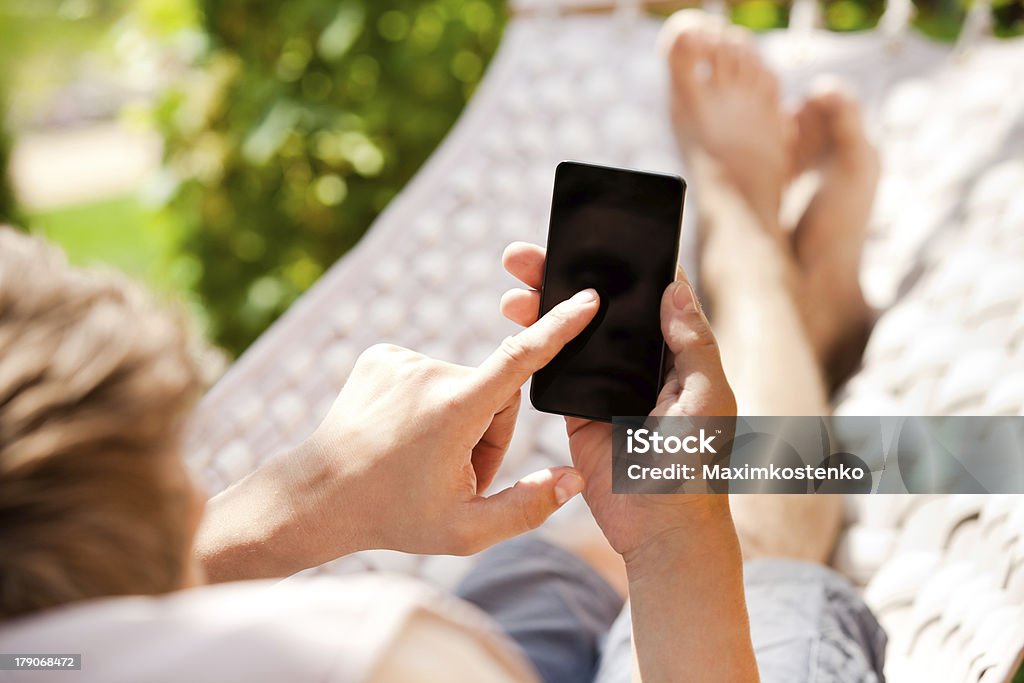 Man using mobile smart phone while relaxing in a hammock Hammock Stock Photo