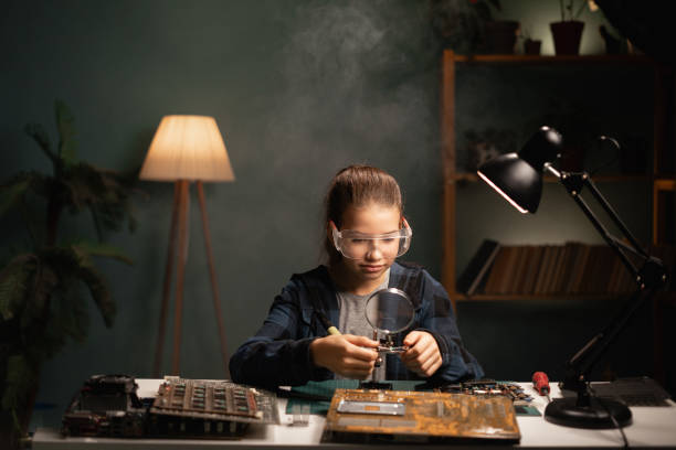 女子学生ははんだごてを使用しています。彼女はコンピュータを修理しています。ハードウェア工学、技術、科学 - table optical instrument metal steel ストックフォトと画像