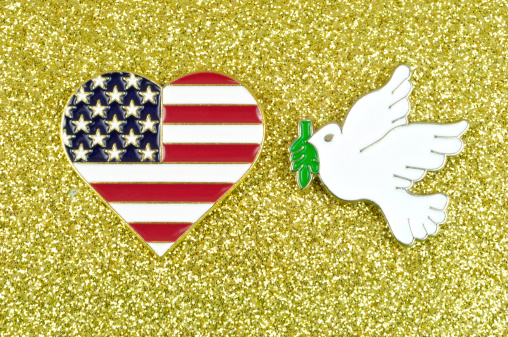 Red stars and stripes love heart with white dove of peace carrying olive branch on a glittering gold background.